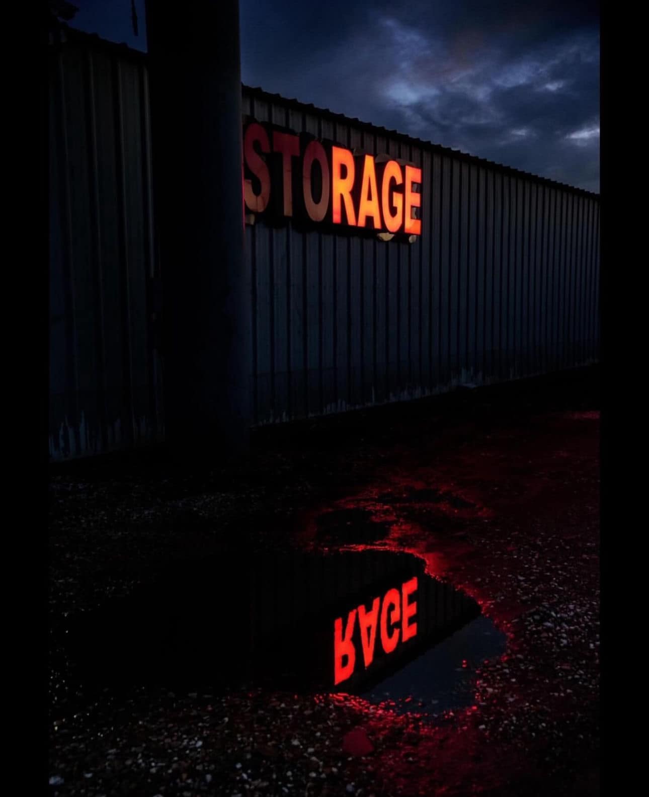 Okay, let's break down this image with the requested analytical lenses. **Visual Description** The image is a low-angle, dramatic shot of a corrugated metal wall with the word "STORAGE" in illuminated, red lettering....