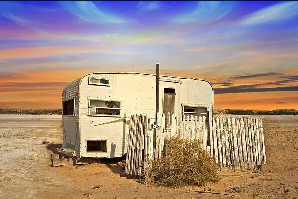 Okay, let's break down this image through the lens of several theoretical frameworks. It's a rich image with plenty to unpack. ## Visual Description The image depicts a dilapidated, vintage travel trailer (or camper)...