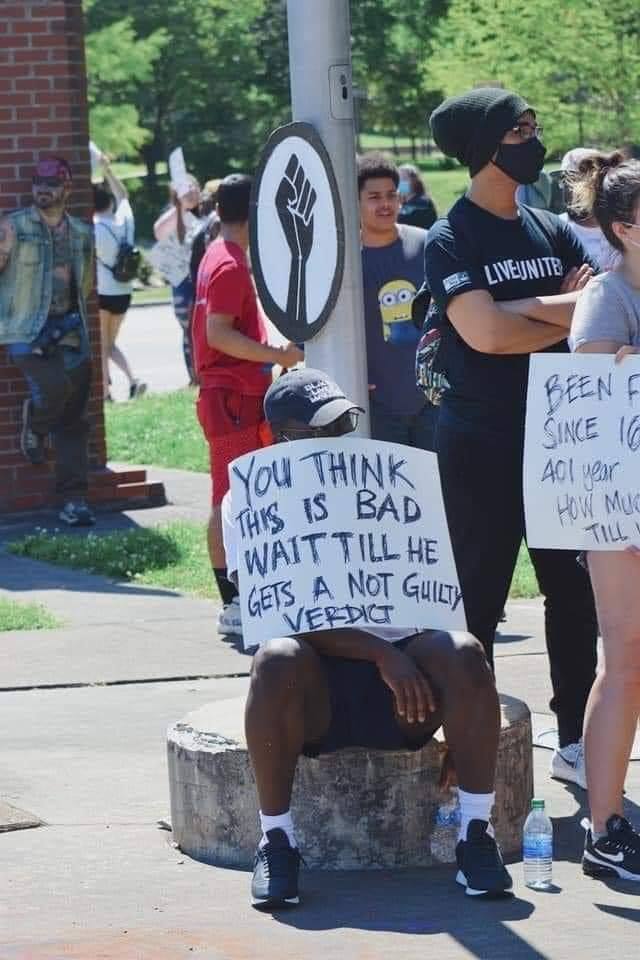 Okay, let's break down this image through the lenses you've requested. I'll note if a specific lens *doesn't* strongly apply. **Image Description** The photo depicts a Black man sitting atop a stone pillar or pedestal...