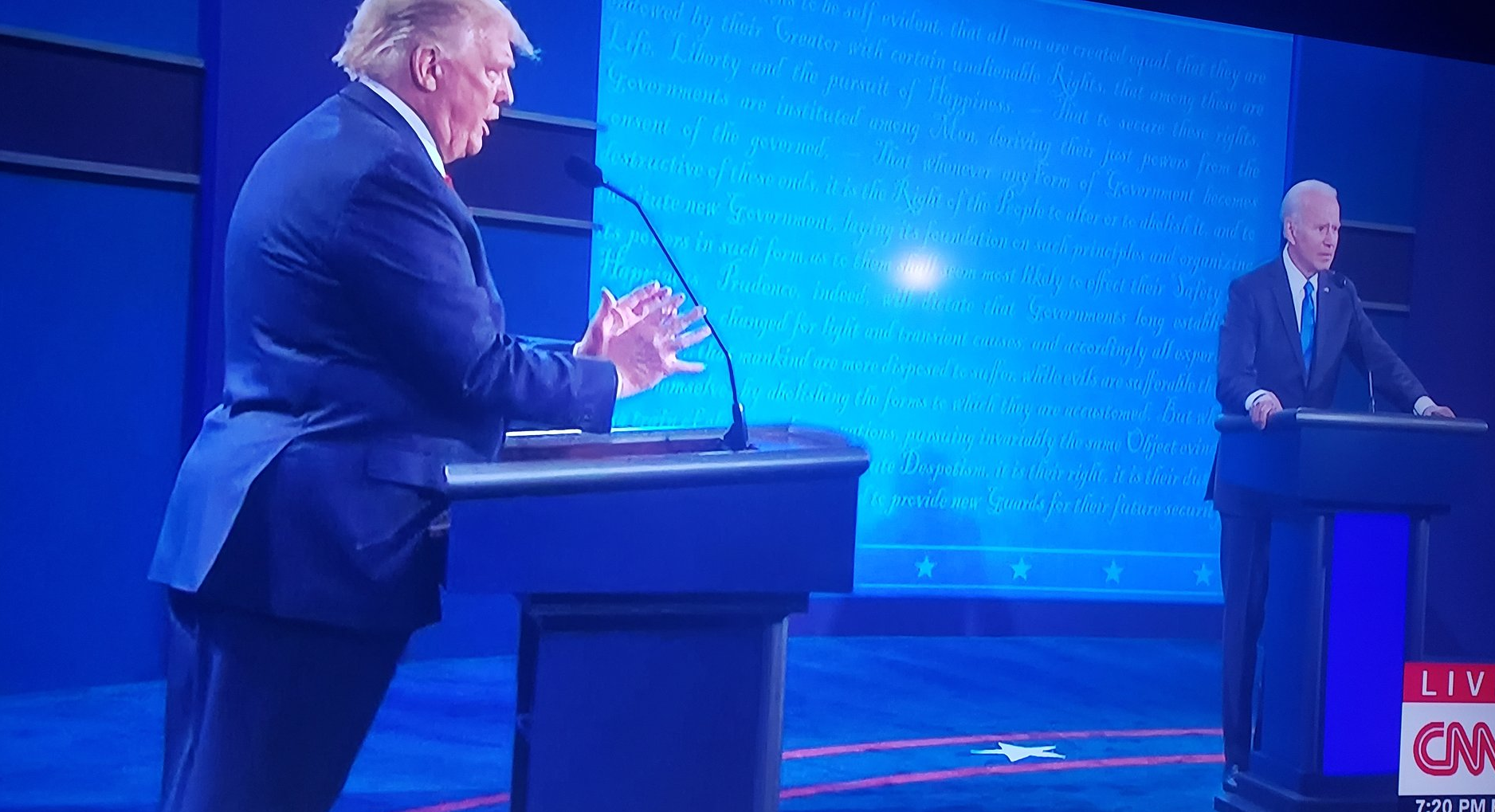 Here's an analysis of the image, broken down into sections as requested. I will only include sections that are demonstrably relevant to the image. **Visual Description** The image shows a political debate setting. Don...