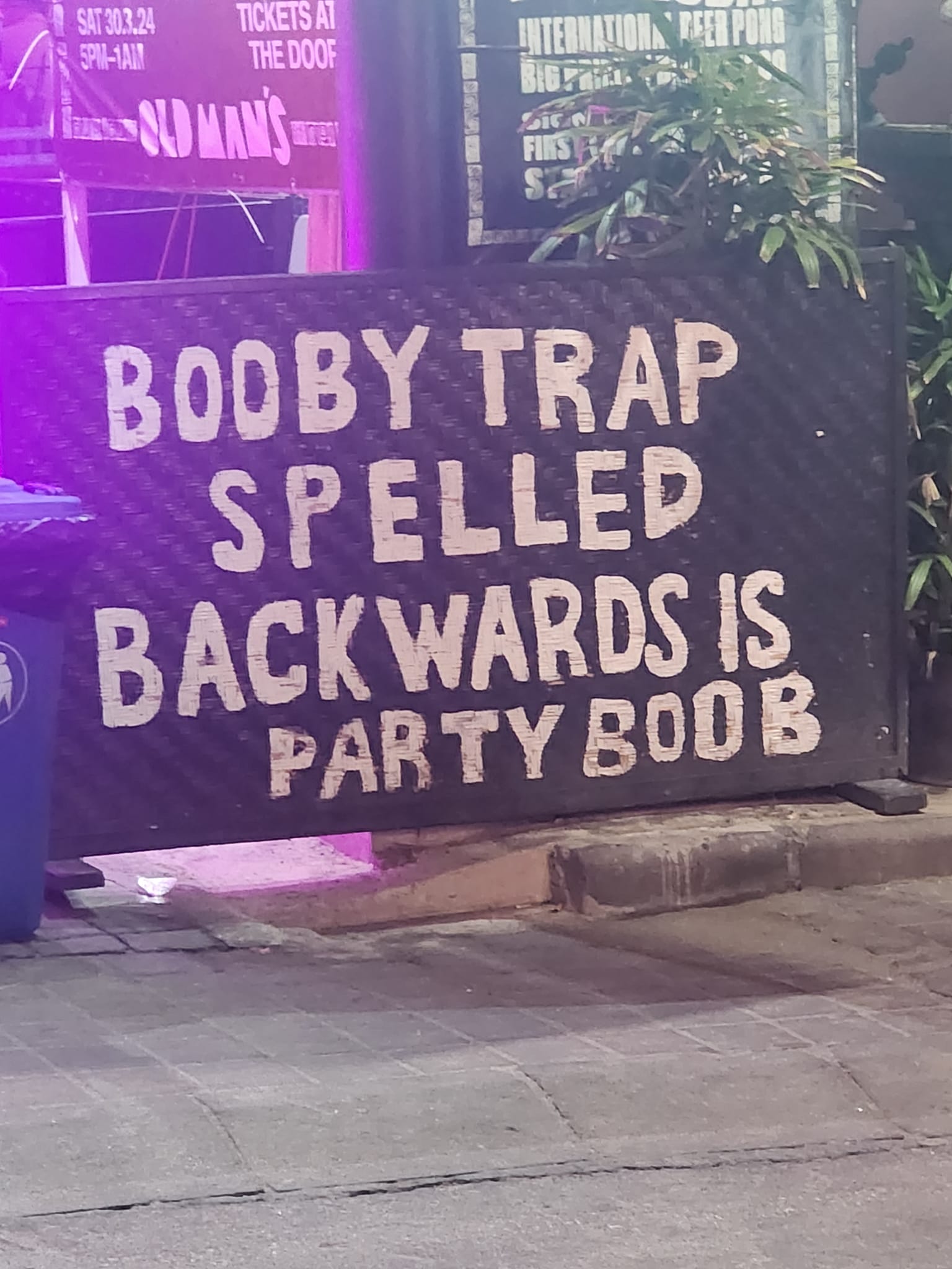 Okay, let's break down this image with the requested theoretical lenses. **Visual Description** The image depicts a sign painted in white lettering on a dark, possibly metallic, surface. The text reads: "BOOBY TRAP SP...