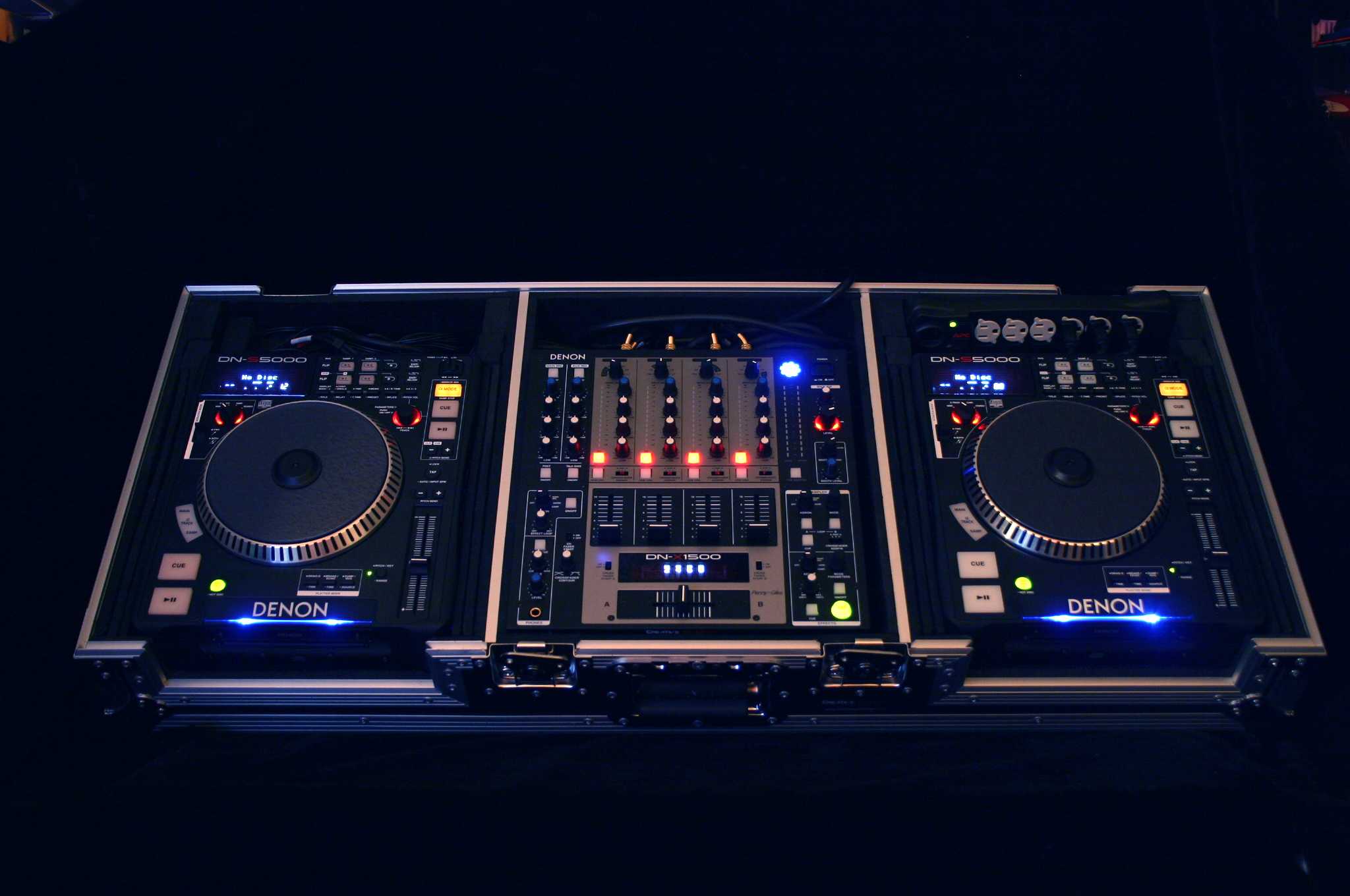 Okay, let's break down the image of the DJ setup through the lenses of various theoretical frameworks. **Visual Description** The image depicts a professional DJ setup in a very dark environment, likely a club or perf...