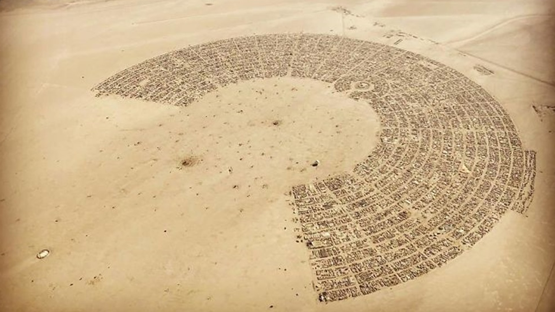 Okay, let's break down this image through several theoretical lenses. This appears to be an aerial photograph of Black Rock City, the temporary settlement erected annually for the Burning Man festival in Nevada’s Blac...
