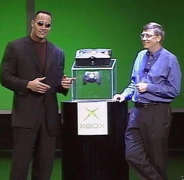 Okay, let's break down this image of Dwayne "The Rock" Johnson and Bill Gates presenting the original Xbox, examining it through several theoretical lenses. **Visual Description** The image depicts Dwayne "The Rock" J...
