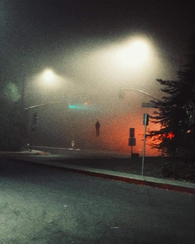 Okay, let's break down this image through various theoretical lenses. **Visual Description** The image presents a nighttime urban scene, heavily atmospheric and obscured by what appears to be fog, smoke, or heavy rain...