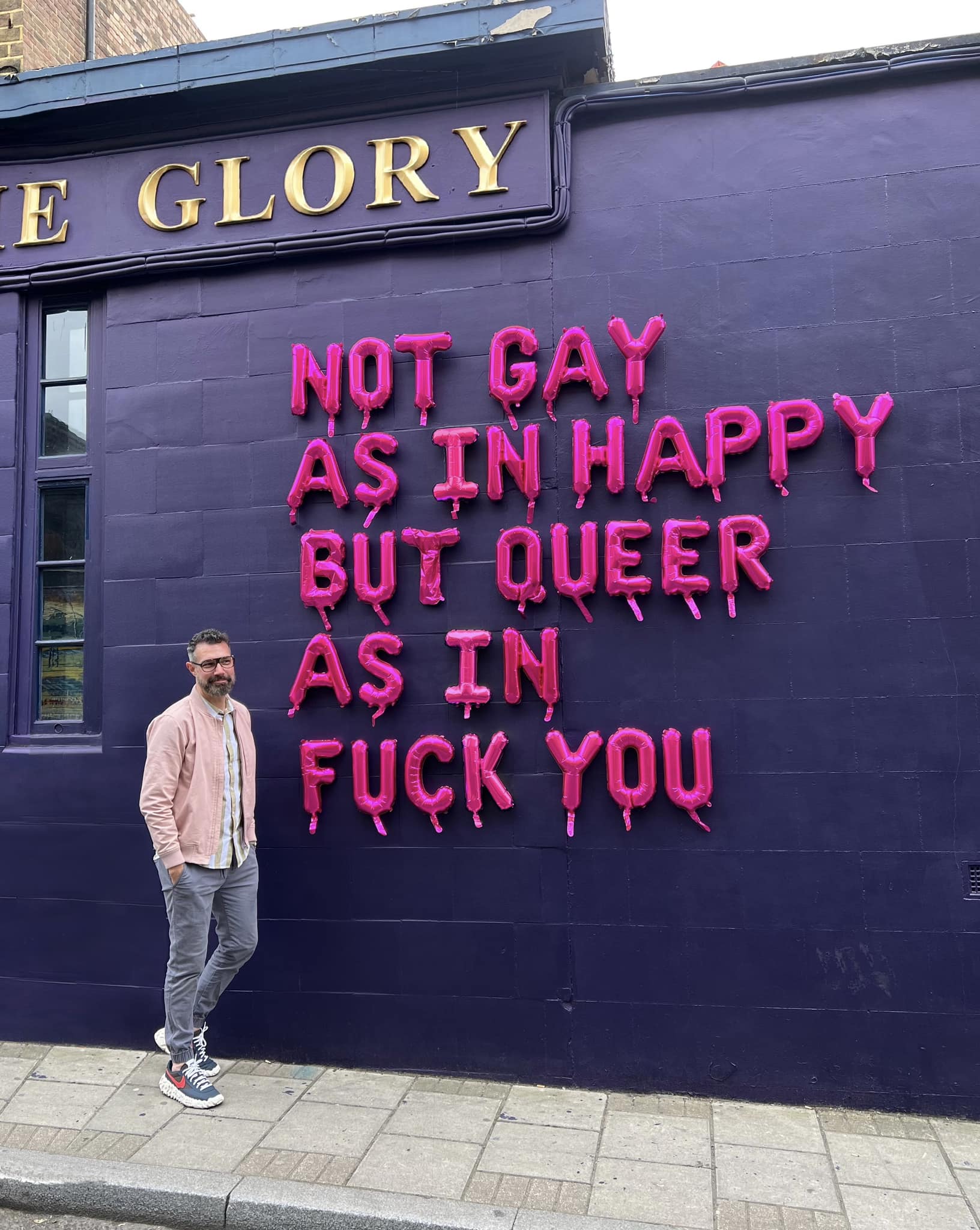 Okay, here's an analysis of the image, broken down into the requested sections. I'll indicate where a section isn't strongly applicable. ## Visual Description The image shows a man standing in front of a vibrant, neon...