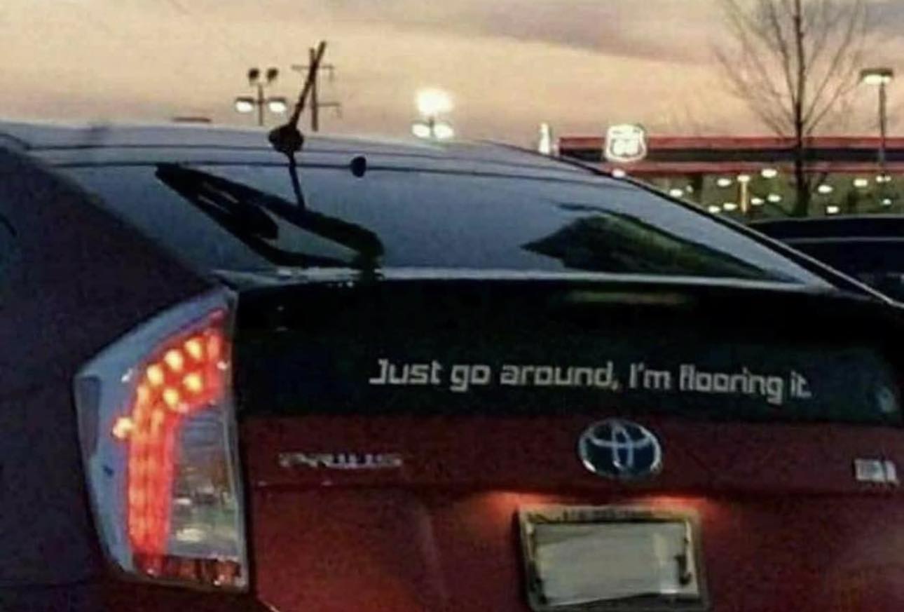 Okay, let's break down the image of the Prius with the bumper sticker "Just go around, I'm flooring it," through the lenses of the requested theoretical frameworks. Not every framework will apply strongly, and I'll ex...